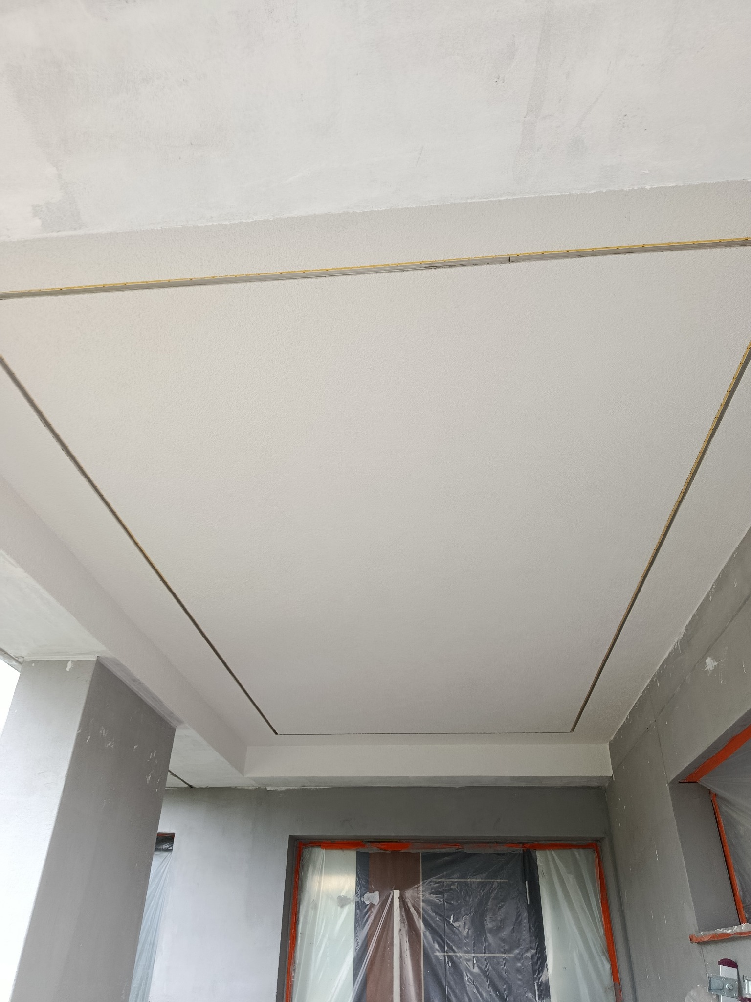 Wykończony sufit podwieszany z listwami LED w nowym budynku. Świeżo położona gładź szpachlowa na suficie. Widoczne zabezpieczone okna folią malarską.