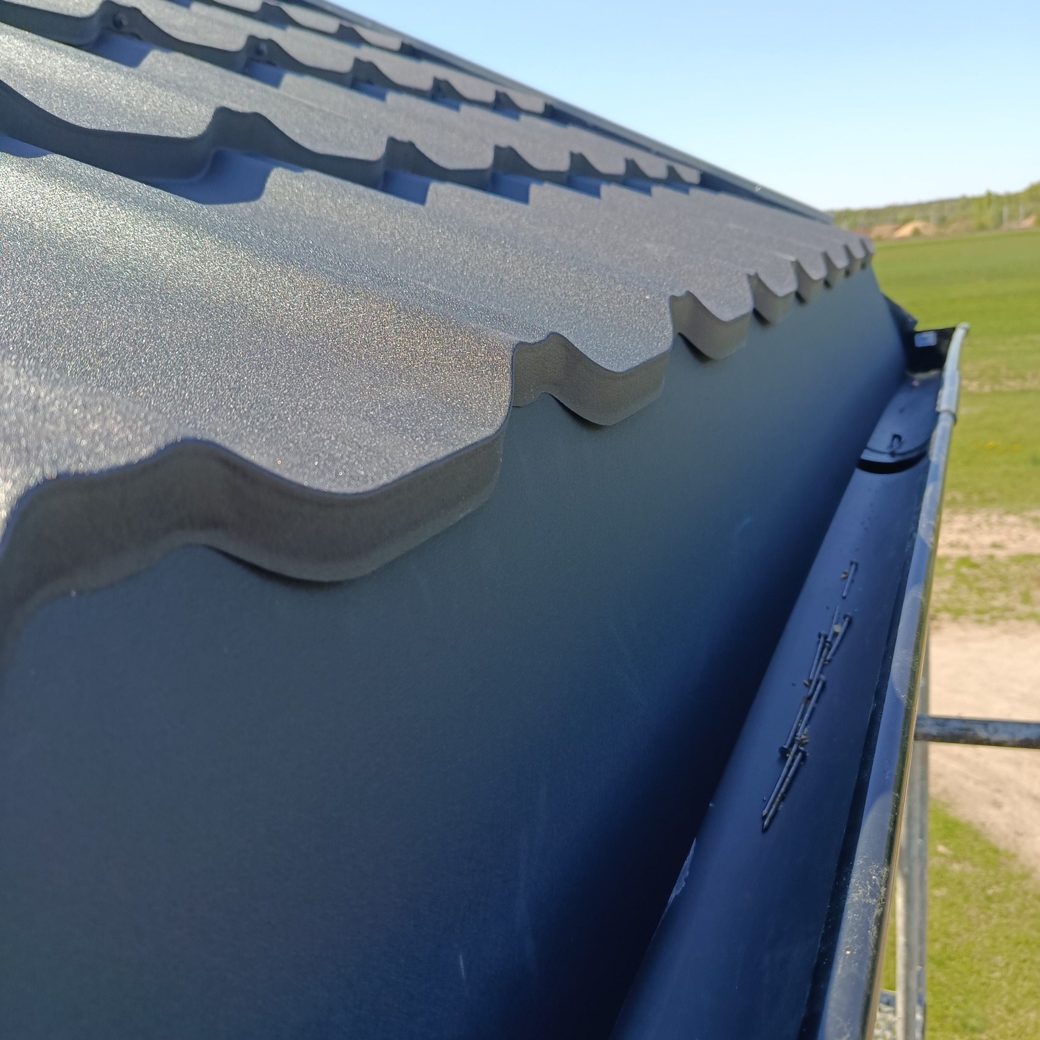 Nowe, metalowe pokrycie dachowe w Błędnicy z bliska, z widocznym systemem rynnowym i estetycznym wykończeniem krawędzi. Dachówka w kolorze grafitowym.