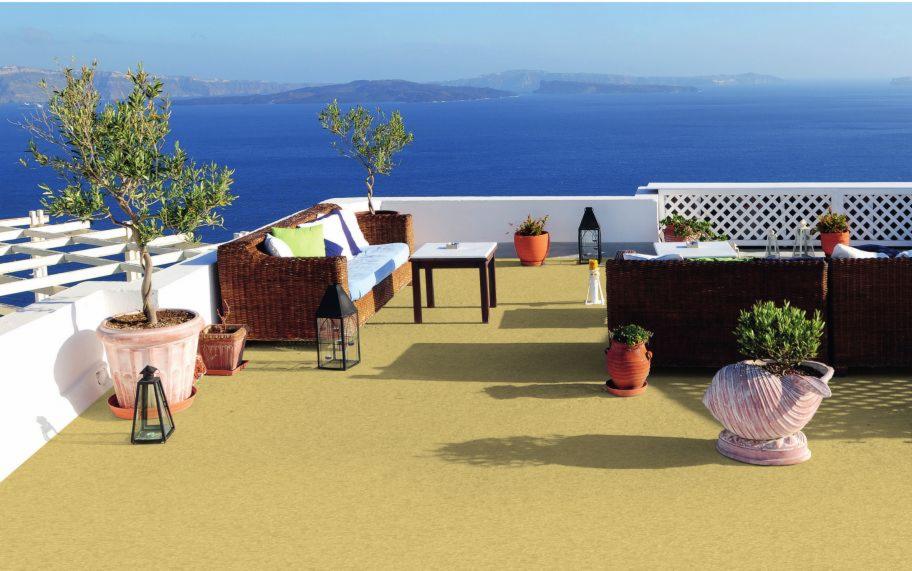 Umeblowany balkon z widokiem na morze, dwie sofy z wikliny z jasnymi poduszkami, stolik kawowy, liczne donice z roślinami, lampiony dekoracyjne, podłoga wyłożona wykładziną w kolorze piaskowym.