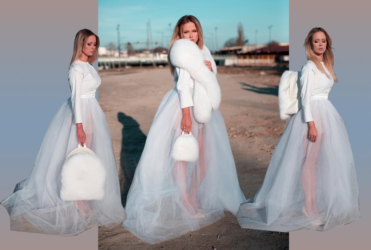 Kobieta w tiulowej spódnicy, futrzanym szalu i torebce na tle piaszczystego krajobrazu z budynkami w oddali, potrójna ekspozycja.