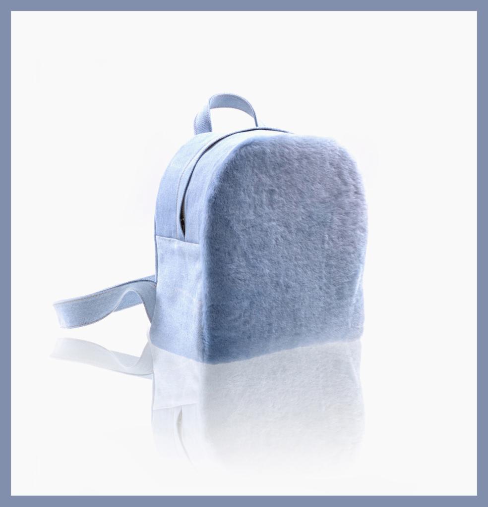 Mały, błękitny plecak z miękkiego, futerkowego materiału, z delikatnym odbiciem na białym tle.