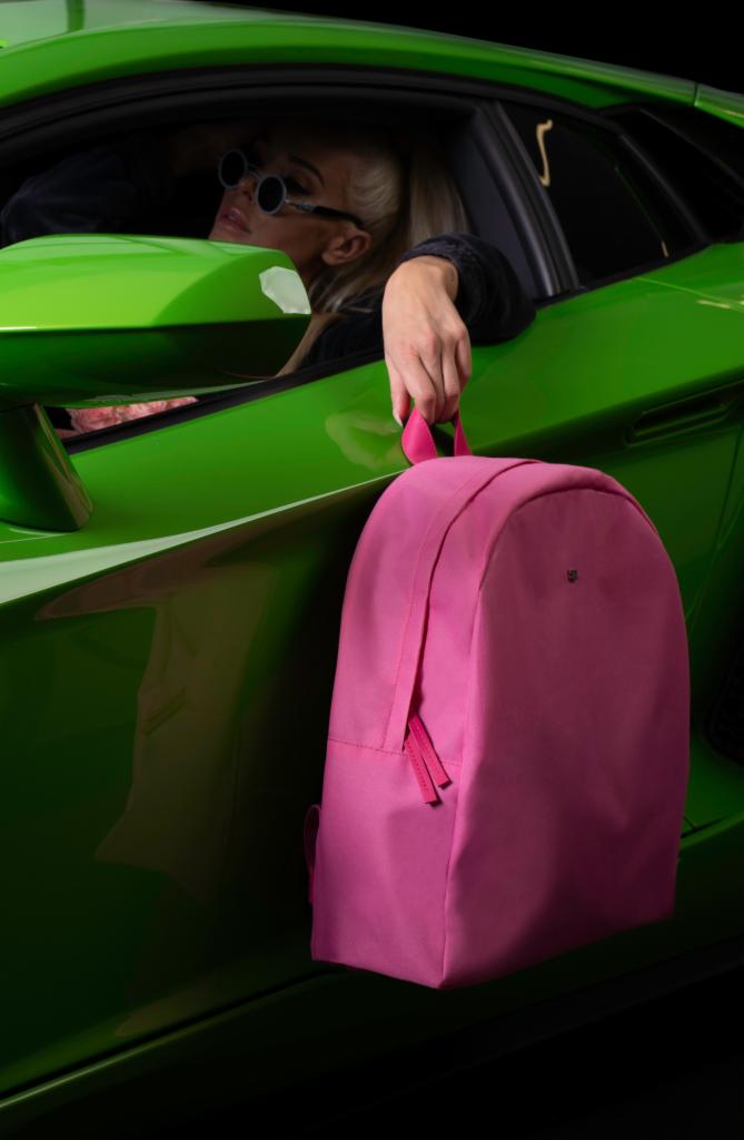 Kobieta w okularach w zielonym Lamborghini trzyma różowy plecak.