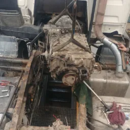 Brudny silnik ciężarówki zawieszony na łańcuchach podczas wymiany, widoczne narzędzia i elementy konstrukcyjne pojazdu.