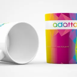 Dwa białe kubki z nadrukiem logo firmy 'adatto' w kolorach tęczy oraz abstrakcyjnego wzoru z trójkątów, jeden kubek leży na boku.