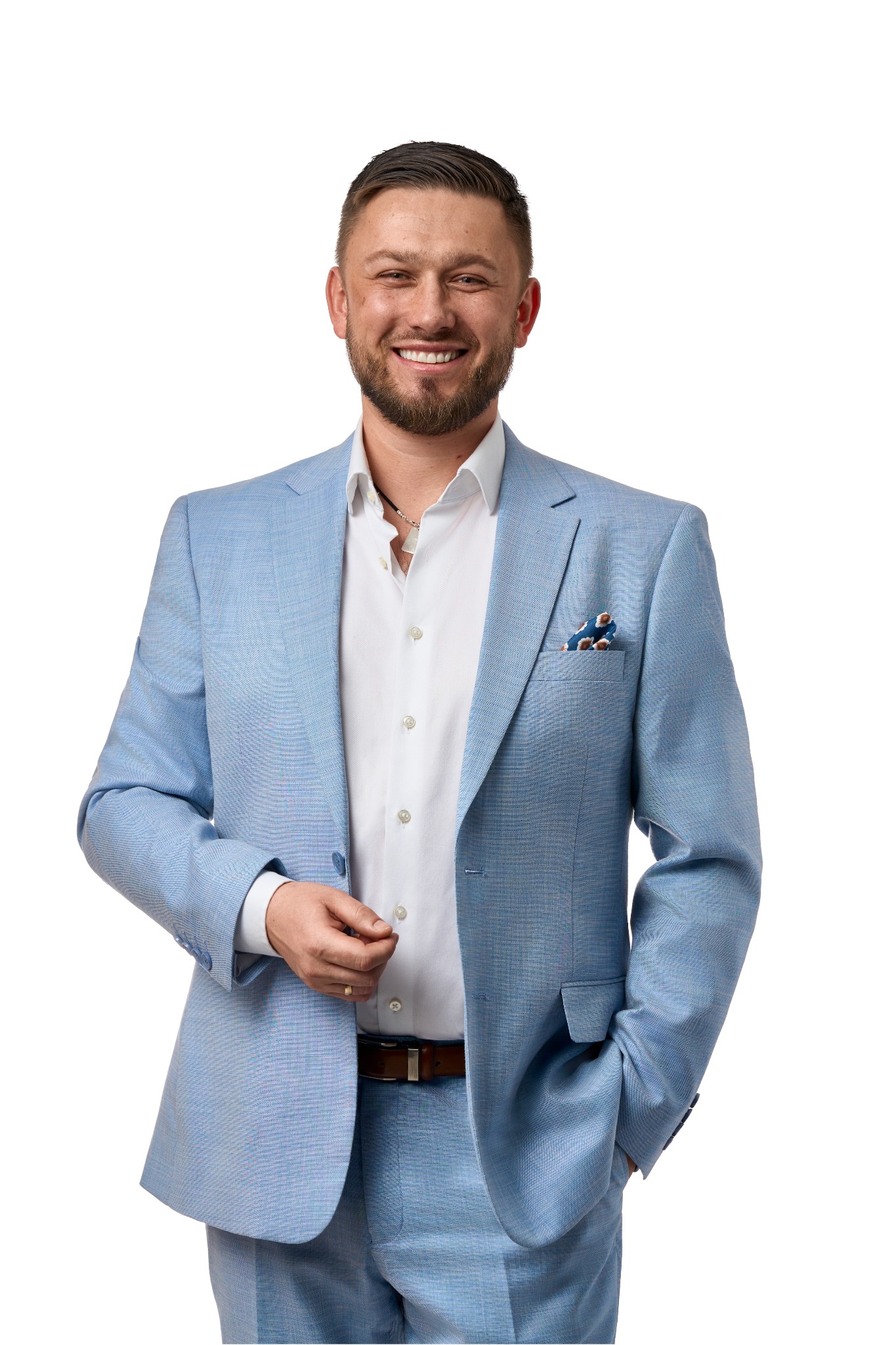 Uśmiechnięty mężczyzna w błękitnym garniturze, białej koszuli i brązowym pasku, na białym tle. Widoczny fragment łańcuszka.