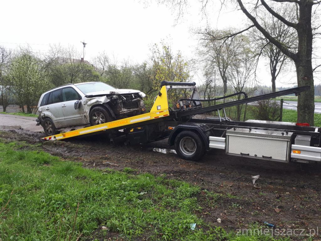 Uszkodzony srebrny SUV na żółtej lawecie w błotnistym terenie, widoczne uszkodzenia przodu pojazdu.