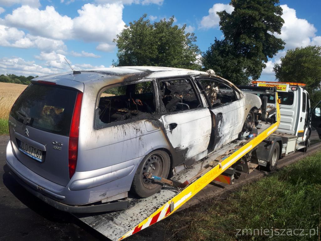Uszkodzony, spalony samochód osobowy Citroen C5 kombi, załadowany na lawetę pomocy drogowej. Widoczne wypalone wnętrze i zniszczona karoseria. Tło stanowią pola i drzewa pod błękitnym, lekko...