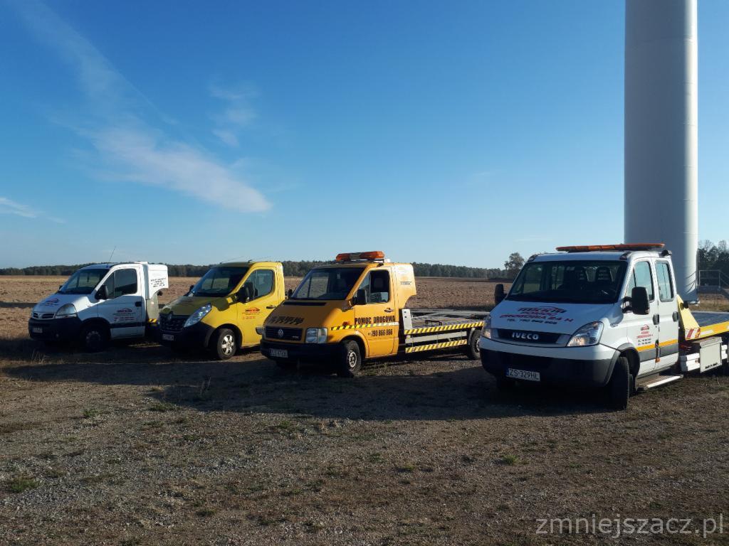 Cztery lawety różnych marek (Iveco, Volkswagen i inne) zaparkowane na polu w słoneczny dzień, na tle wiatraka.