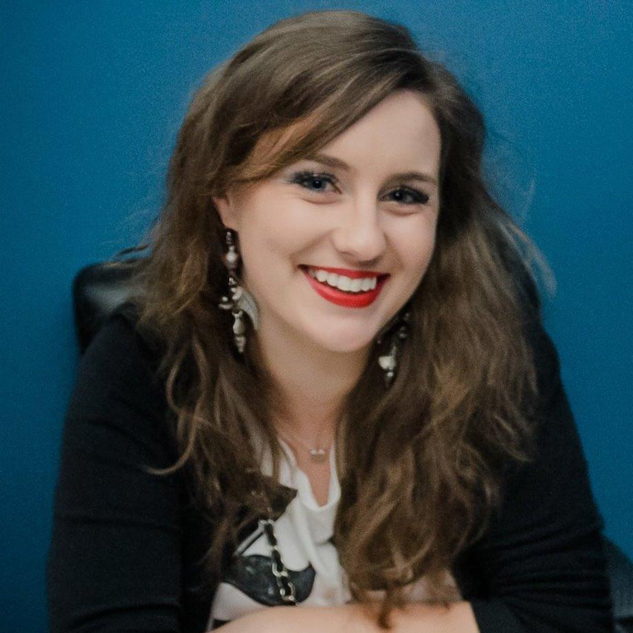 Portret uśmiechniętej kobiety z długimi włosami i wyrazistą czerwoną szminką na tle błękitnej ściany, oferującej usługi tłumaczeń w Rumi.