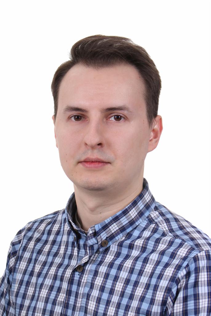 Portret mężczyzny w niebieskiej koszuli w kratę na białym tle. Ujęcie od przodu, skupione na twarzy i górnej części torsu. Neutralny wyraz twarzy, stonowane oświetlenie.