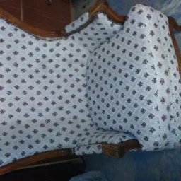 Antyczny fotel po renowacji, z drewnianą ramą i tapicerką w drobny kwiatowy wzór, widoczne detale wykończenia i nóżki.