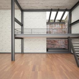 Kinvest - Wnętrze w stylu loft z drewnianą podłogą, białą cegłą na ścianach i stalową konstrukcją antresoli z balustradą i schodami.