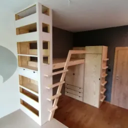Drewniana antresola z zabudową szafy i regału, połączona drabinką, w pokoju z ciemną ścianą.