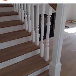 Jasne drewniane stopnie schodów z białymi podstopnicami i balustradą, widok z góry, minimalistyczny design.