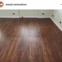 Ułożona podłoga z ciemnego drewna, widoczne listwy przypodłogowe i gniazdka elektryczne na ścianie.