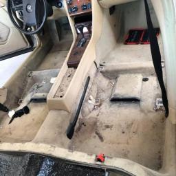 Steam Perfect Damian Piątek - Wnętrze starego samochodu marki Mercedes przed czyszczeniem: brudna tapicerka podłogowa, widoczne narzędzia w schowku pasażera, beżowe elementy deski rozdzielczej.