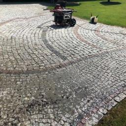 Steam Perfect Damian Piątek - Czyszczenie kostki brukowej z użyciem myjki ciśnieniowej, widoczne zabrudzenia i woda na powierzchni, wzór z czerwonej kostki.