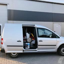 Steam Perfect Damian Piątek - Srebrny van z otwartymi drzwiami bocznymi i tylnymi, widoczne wyposażenie do czyszczenia wewnątrz, zaparkowany na kostce brukowej przed szarym budynkiem.