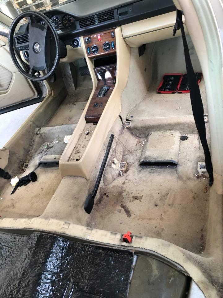 Wnętrze starego samochodu marki Mercedes przed czyszczeniem: brudna tapicerka podłogowa, widoczne narzędzia w schowku pasażera, beżowe elementy deski rozdzielczej.