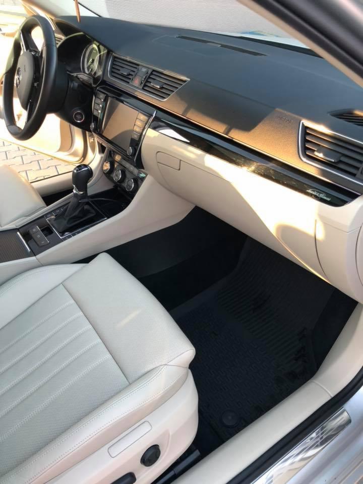 Wnętrze samochodu Skoda Superb po detailingu, widoczne jasne skórzane fotele z perforacją, czarne gumowe dywaniki i deska rozdzielcza z elementami czerni fortepianowej.