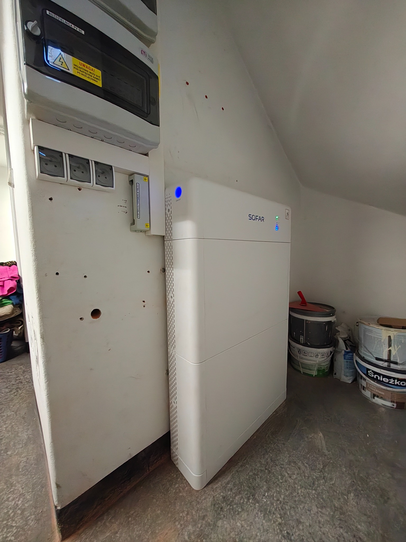 Bateria SOFAR i rozdzielnica PV DC w Lublińcu. Widoczne gniazdka i listwa wyrównania potencjału. Instalacja fotowoltaiczna w pomieszczeniu ze skośnym sufitem.