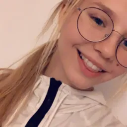 Uśmiechnięta blondynka w okularach, z filtrem serduszek, ubrana w białą bluzę z czarnym zamkiem.