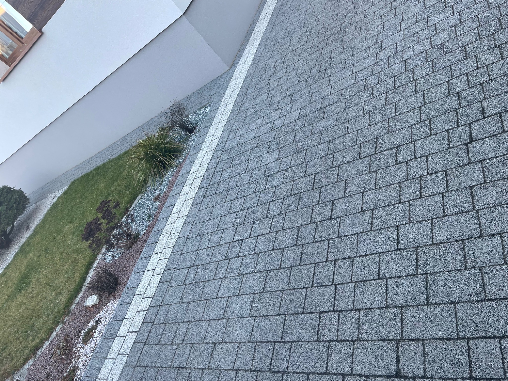 Nietypowy kadr z góry na ułożoną szarą kostkę granitową w Gniewkowie, z widocznym fragmentem trawnika i ozdobnych kamieni wzdłuż ściany budynku.