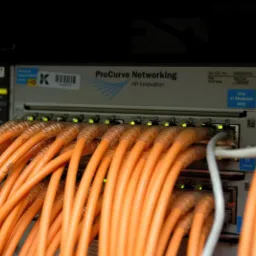 Switch sieciowy ProCurve Networking HP Innovation z pomarańczowymi kablami Ethernet, zainstalowany w serwerowni w Kielcach. Na kablach widoczne napisy 'FIREWALL 16 LAN'.