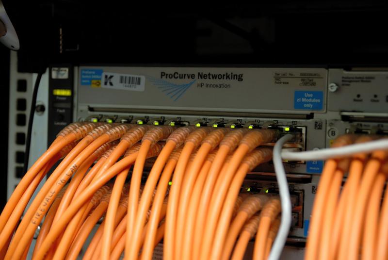 Switch sieciowy ProCurve Networking HP Innovation z pomarańczowymi kablami Ethernet, zainstalowany w serwerowni w Kielcach. Na kablach widoczne napisy 'FIREWALL 16 LAN'.