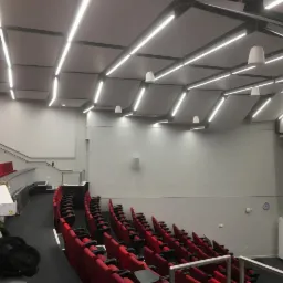 Sala wykładowa z czerwonymi fotelami i zamontowanymi panelami akustycznymi na suficie z oświetleniem LED.