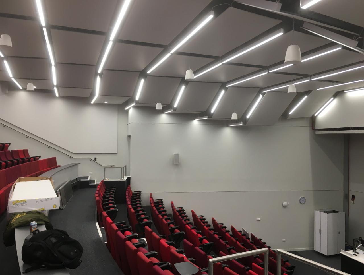 Sala wykładowa z czerwonymi fotelami i zamontowanymi panelami akustycznymi na suficie z oświetleniem LED.