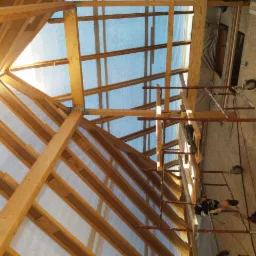 Konstrukcja drewniana dachu w trakcie budowy, widoczne rusztowania i folia izolacyjna, jasne drewno i metalowe łączniki.