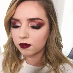 Portret kobiety z zamkniętymi oczami, prezentującej bordowy odcień szminki i błyszczący, miedziano-bordowy cień do powiek z efektem cut crease.