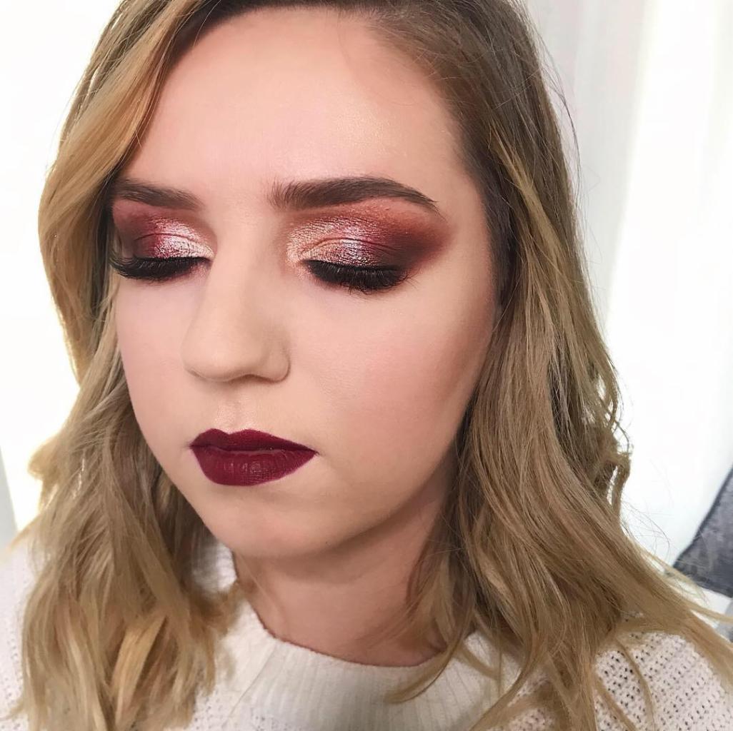 Portret kobiety z zamkniętymi oczami, prezentującej bordowy odcień szminki i błyszczący, miedziano-bordowy cień do powiek z efektem cut crease.
