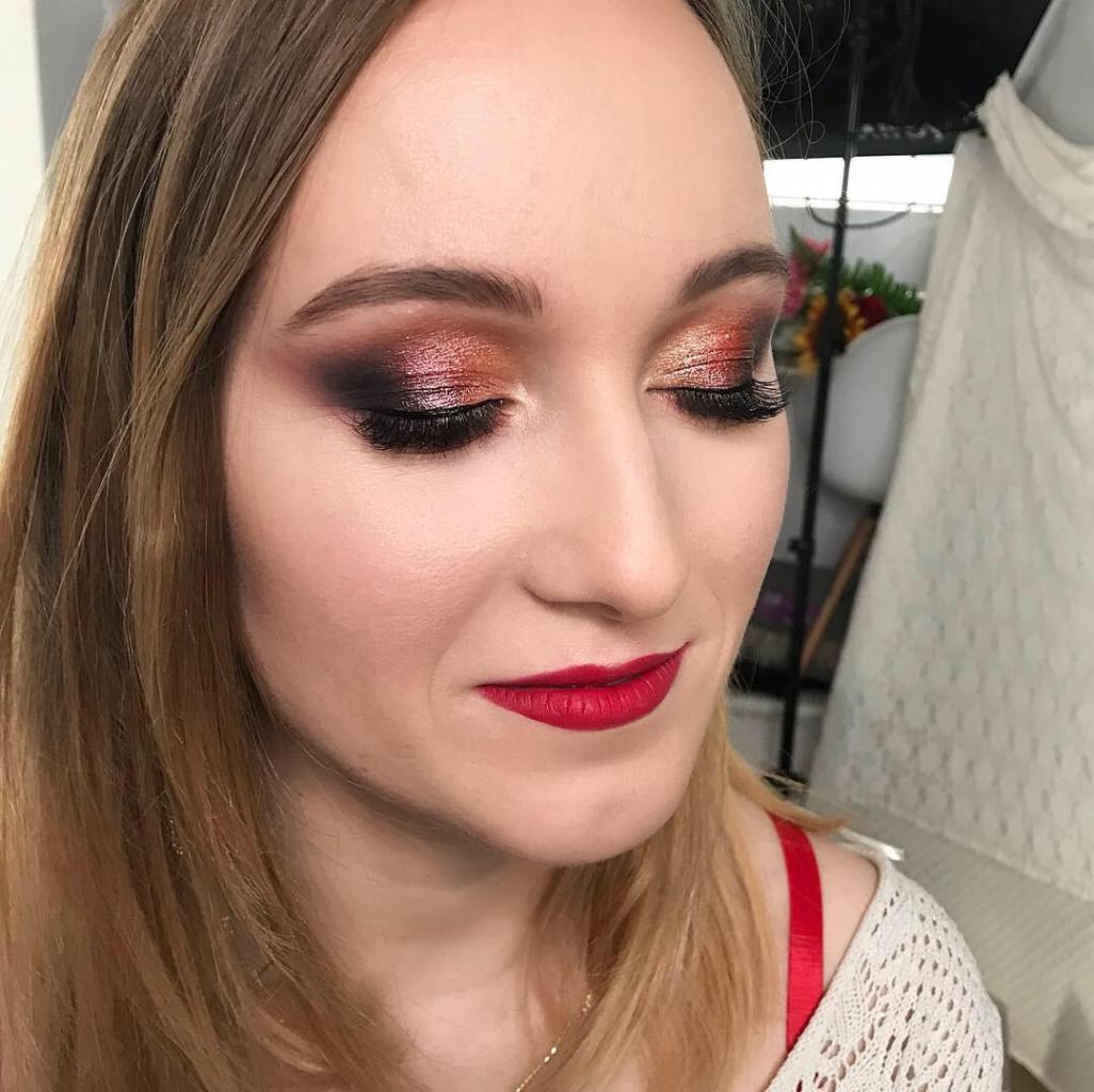 Portret kobiety z zamkniętymi oczami, prezentujący intensywny, metaliczny cień do powiek w odcieniach brązu i pomarańczy oraz wyraziste, czerwone usta.