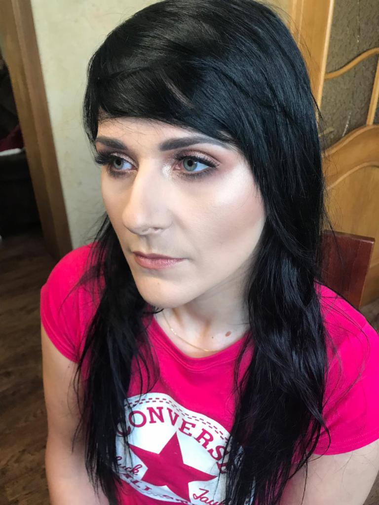 Portret kobiety z delikatnym, rozświetlonym efektem na skórze, wykonanym w Dobrzeniu Małym. Widoczne podkreślone oczy i brwi oraz subtelnie zaznaczone usta. Uwagę zwraca intensywnie różowa koszulka...