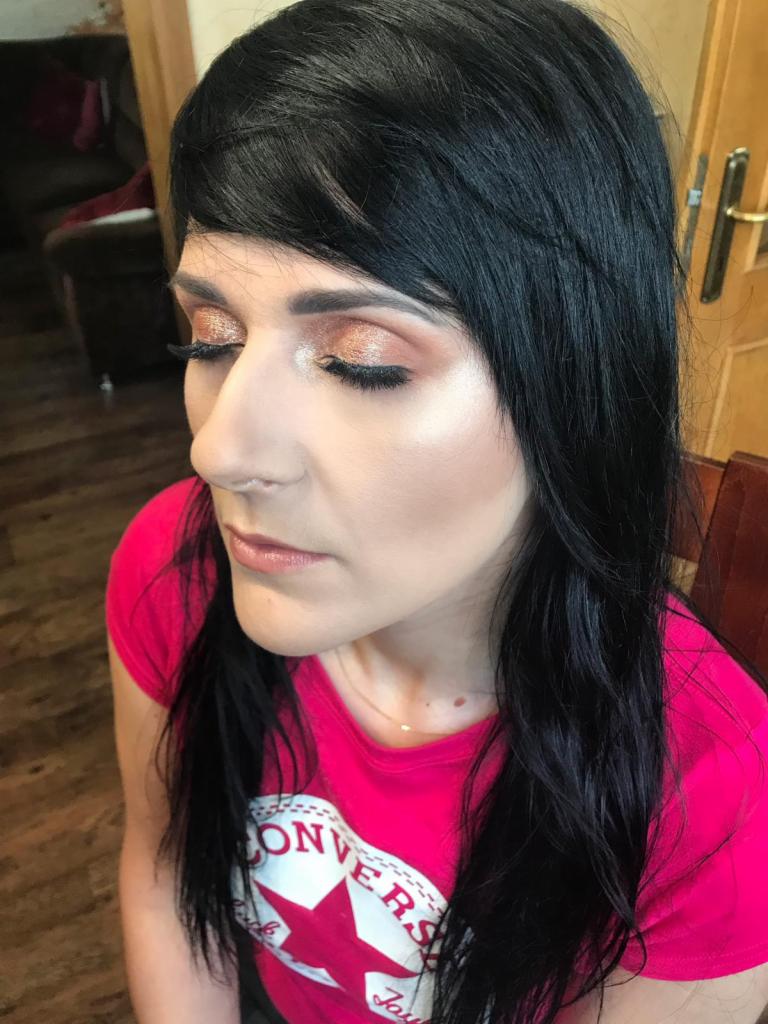 Portret kobiety z ciemnymi włosami i błyszczącym, brzoskwiniowym cieniem do powiek, sztuczne rzęsy i delikatny makijaż ust. Ubrana w różową koszulkę z logo Converse.