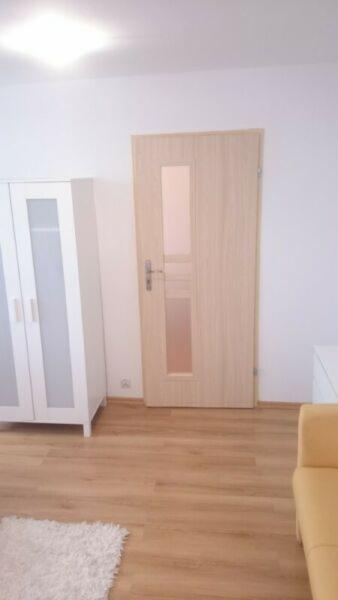 Jasne, drewnopodobne panele podłogowe w pokoju z białą szafą i drzwiami z przeszkleniem, widoczne z poziomu podłogi.