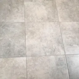 Ułożone kwadratowe panele podłogowe w odcieniach szarości i beżu, z widocznymi fugami, w słabym oświetleniu.