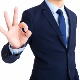 Mężczyzna w granatowym garniturze, błękitnej koszuli i krawacie, pokazuje gest 'OK' na białym tle.