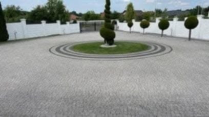 Granitowa nawierzchnia z okrągłym wzorem i zielenią w centrum, Łukta. Biały mur w tle. Widok z perspektywy.