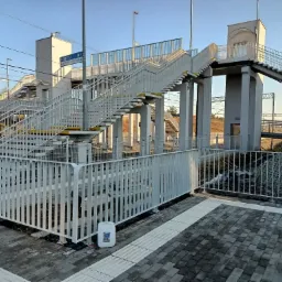 Biała kładka dla pieszych nad torami kolejowymi, świeżo pomalowana, z widocznym kanistrem farby 'NITRO' przy barierce.