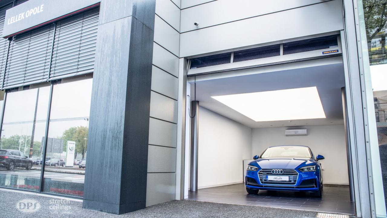 Niebieski samochód Audi w nowoczesnym garażu z podwieszanym sufitem z oświetleniem LED, widok z zewnątrz salonu samochodowego Lellek Opole.