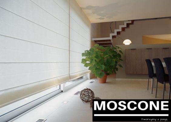 Jasne, poziome panele okienne w minimalistycznym wnętrzu, obok doniczkowa roślina i dekoracyjna kula, schody w tle.