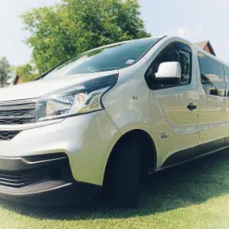 Srebrny bus Fiat z numerem rejestracyjnym DW 1N654, zaparkowany na zielonej trawie przed drzewami, widok z przodu z lekkiego dołu.