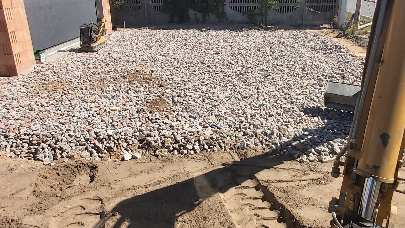 Przygotowanie terenu pod budowę w Zalasewie: ubijarka w tle, grunt częściowo wysypany kamieniem, wykopana ziemia z przodu. Widoczne ślady opon.