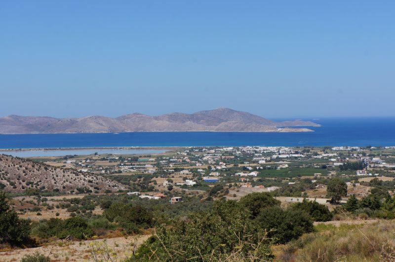 Panoramiczny widok na miasto nadmorskie z oddalonymi górami i błękitnym morzem w tle, oświetlone jasnym światłem słonecznym.