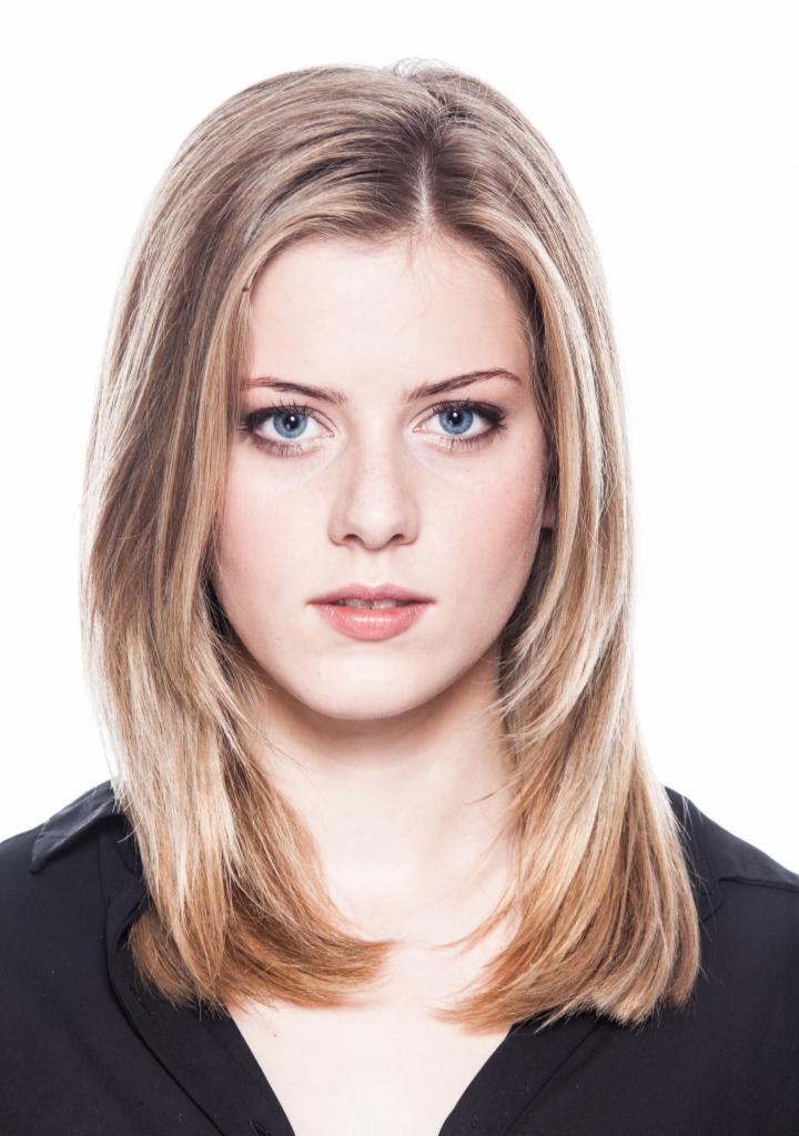 Portret młodej kobiety z blond włosami i niebieskimi oczami, ubrana w czarną koszulę, na białym tle.