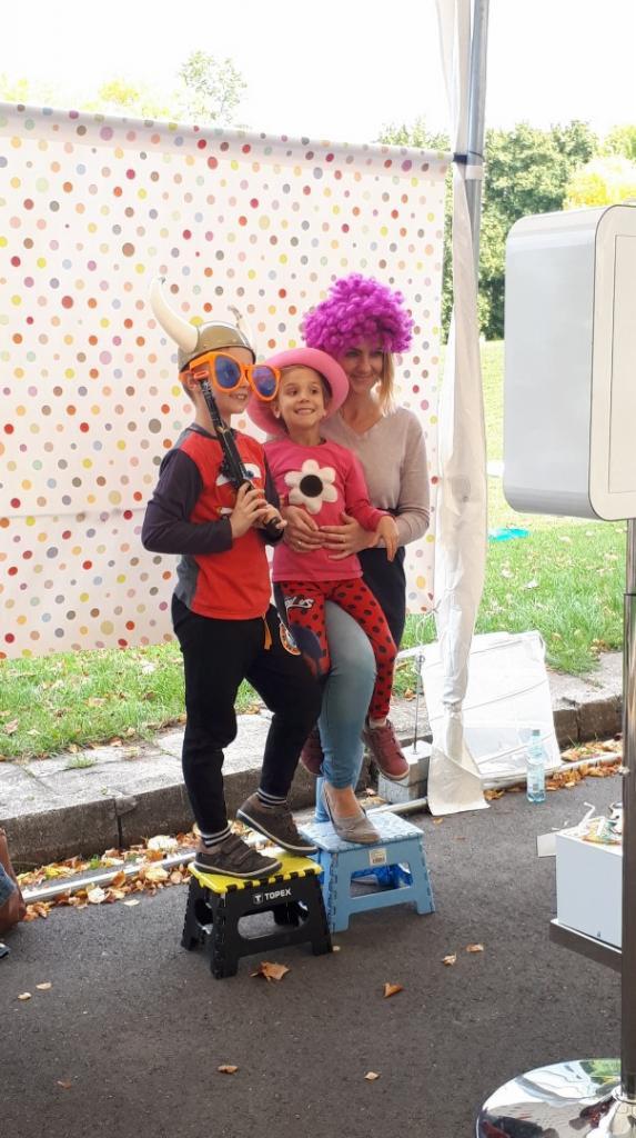 Rodzinne zdjęcie w fotobudce z kolorowym tłem w kropki, dzieci przebrane w peruki i zabawne okulary, chłopiec trzyma plastikowy pistolet.