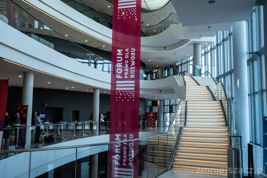 Wnętrze nowoczesnego centrum konferencyjnego z wielopoziomowymi galeriami, schodami z podświetleniem LED i banerem reklamowym 'Forum Prawo dla Rozwoju'.